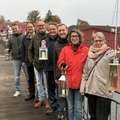 Mehrere Menschen stehen mit Laternen auf einer Holzbrücke.