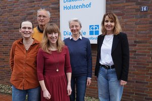 Fünf Menschen vor einem Schild des Diakonischen Werkes Rendsburg-Eckernförde