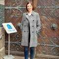 Eine Frau steht im Mantel vor einer Kirche, daneben ein Schild "Die Kirche ist offen"